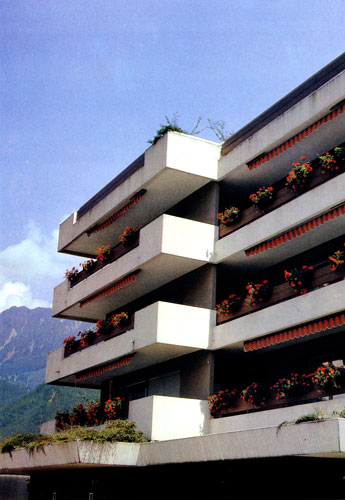 Пример оригинального украшения фасада дома. Ниспадающие пеларгонии (Pelargonium peltatum), растущие на его балконах в цветочных ящиках, гармонируют со шторами, защищающими внутренние помещения от палящих лучей солнца 