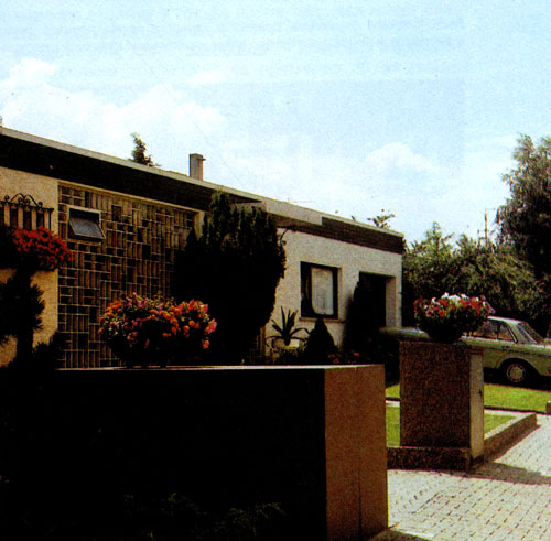 Хорошее решение входа в дом. Каменное корыто в качестве вегетационного сосуда для пеларгоний и крупноцветные ломоносы, вьющиеся по простой конструкции, прикрепленной к стене, — главные элементы украшения 